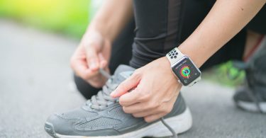 person tying shoes while wearing apple watch outside