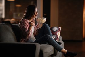 woman watching a movie on her couch eating popcorn