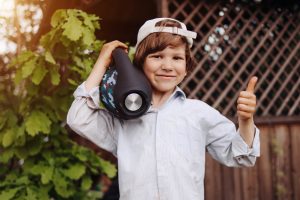 young boy listening to a portable speaker while giving a thumbs up