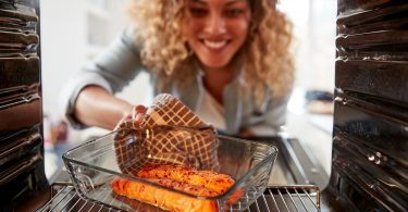 Woman in kitchen pulling cooked salmon out of the oven