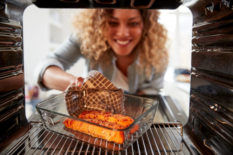Woman in kitchen pulling cooked salmon out of the oven