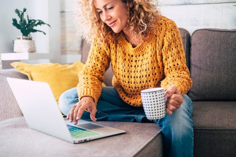 Lady with curly hair in yellow sweater using laptop at home