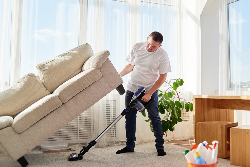 man vacuuming under living room sofa