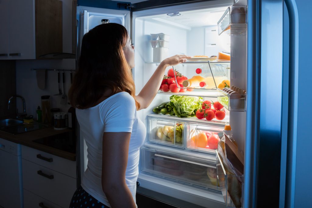 young woman grabbing veggies out of her refrigerator at home