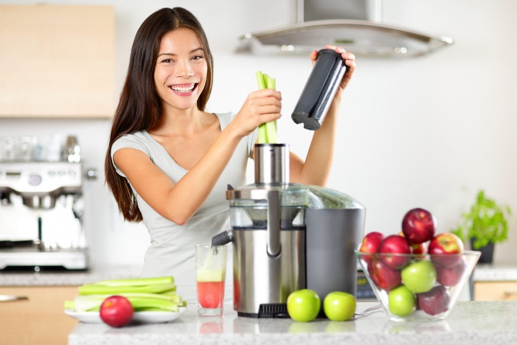 A female using apples and celery to make juice with a juicer