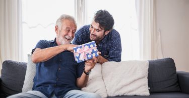 Older man opens gift from his son with a big smile on his face