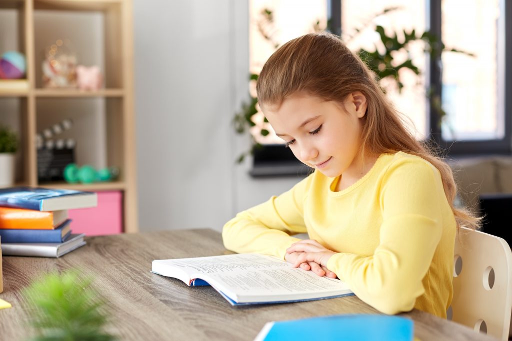 young girl at home studying textbook at her desk 
