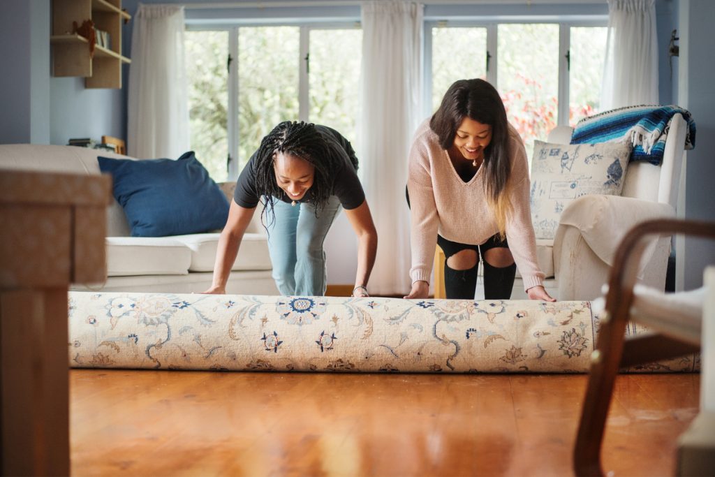 Two women unrolling carpet in new house