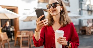 young woman using cell phone in front of cafe