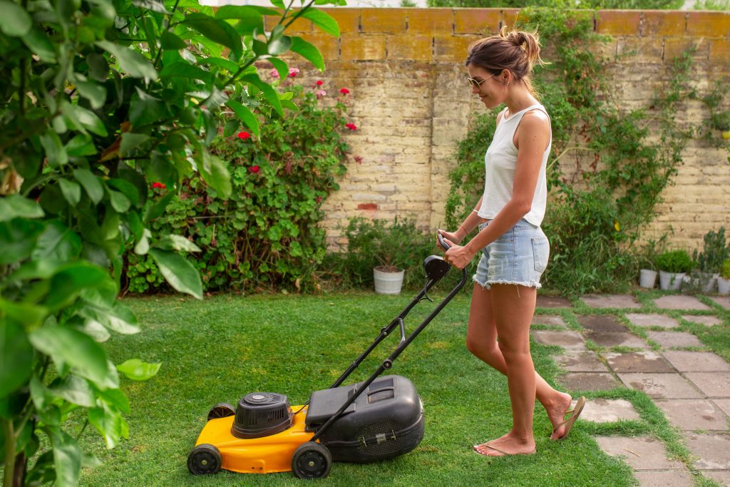 female college student mowing grass in backyard