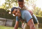 Young Black Boy Playing On Dad Back In A Garden