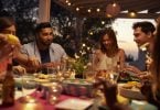 Young adults dining at outdoor party with lights in background