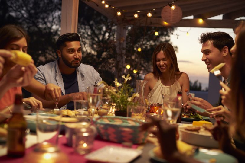 Young adults dining at outdoor party with lights in background