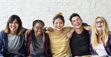 Five-happy-diverse-group-of-high-school-to-college-age-students-sitting-and-smiling-with-arms-around-each-other