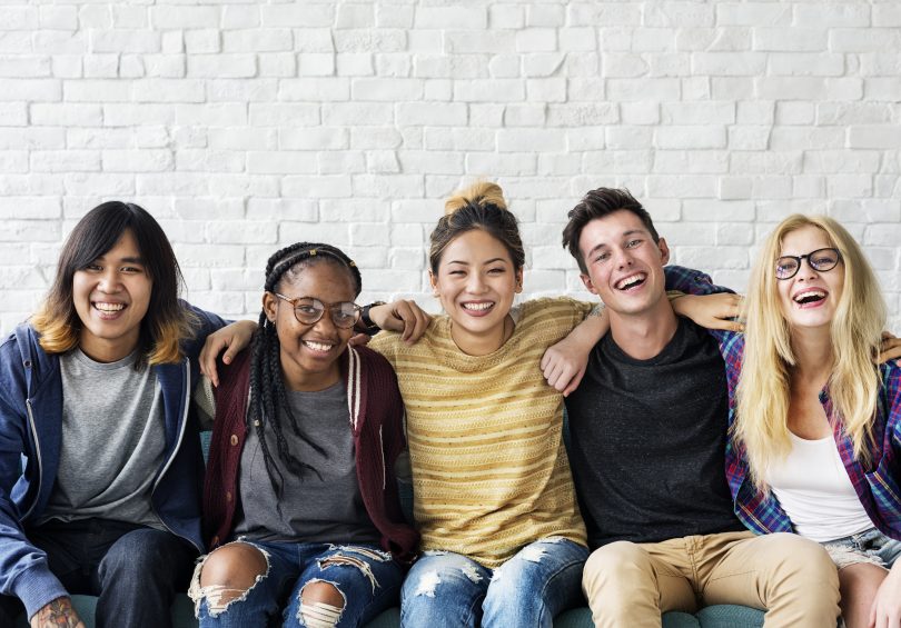 Five-happy-diverse-group-of-high-school-to-college-age-students-sitting-and-smiling-with-arms-around-each-other