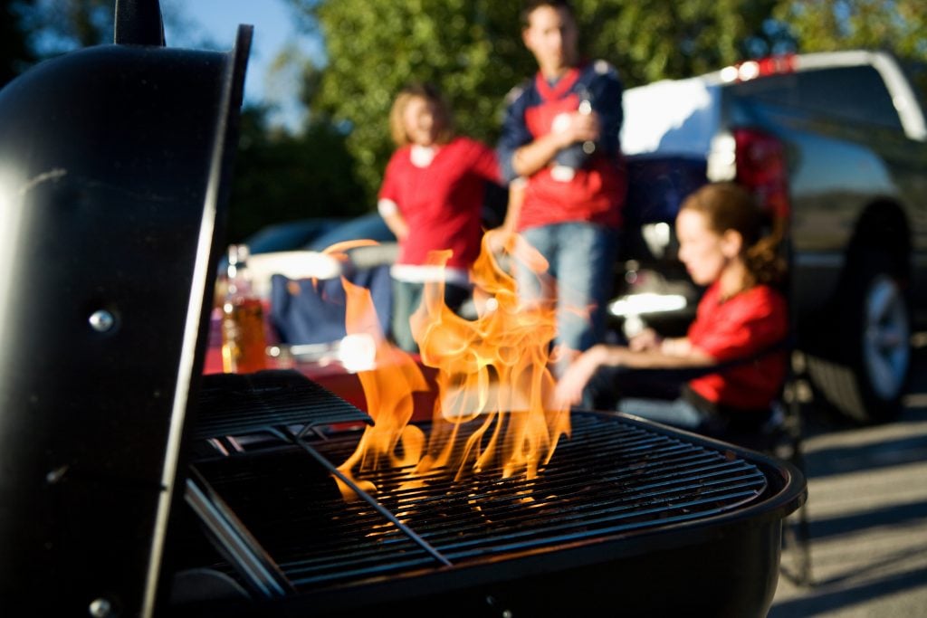 Football tailgating scene with closeup of fiery grill and tailgaters in background