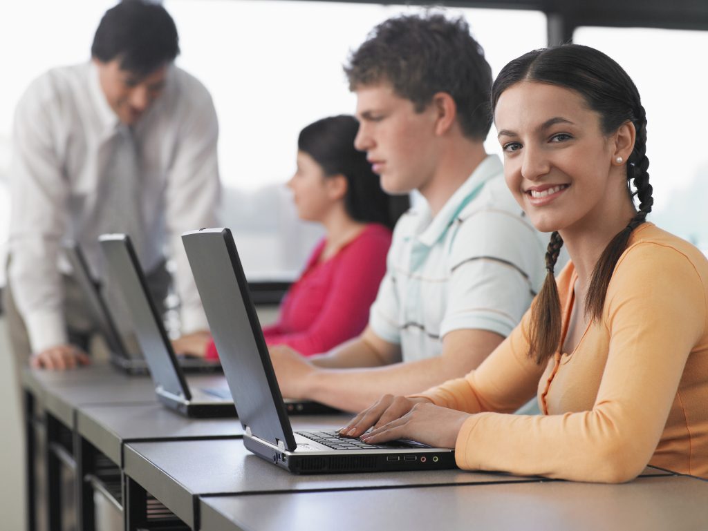 White high-school students with laptops girl in braid smiling at camera