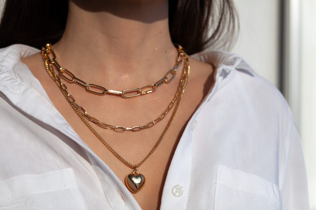 Closeup of woman wearing 3 rose-gold necklaces at neck of white button-up shirt