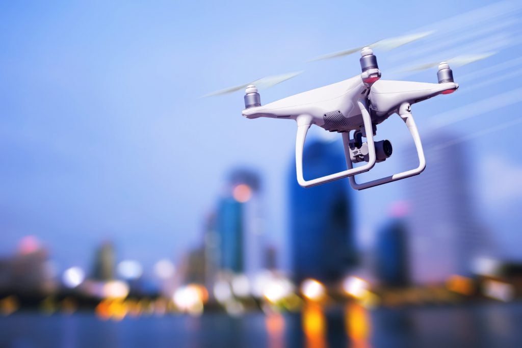 Close-up of white drone against blue sky and blurred lit-up city scape in background
