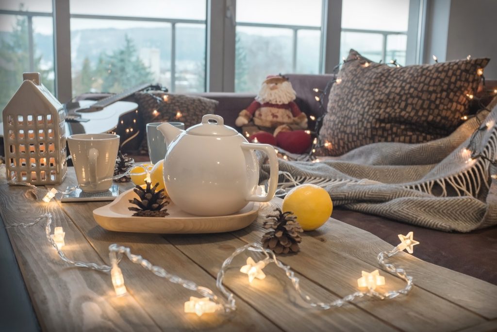 Closeup of a cozy couch and coffee table with string lights, hot tea, fluffy pillows, throws