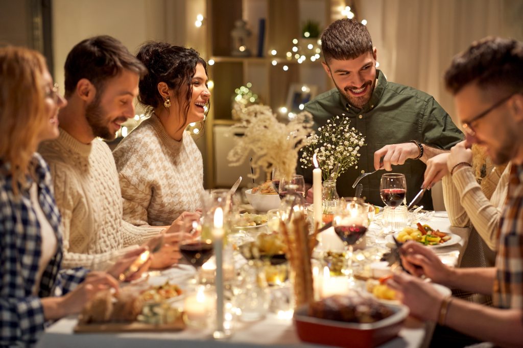 Diverse group of young adults at holiday dinner with candles and twinkle lights around