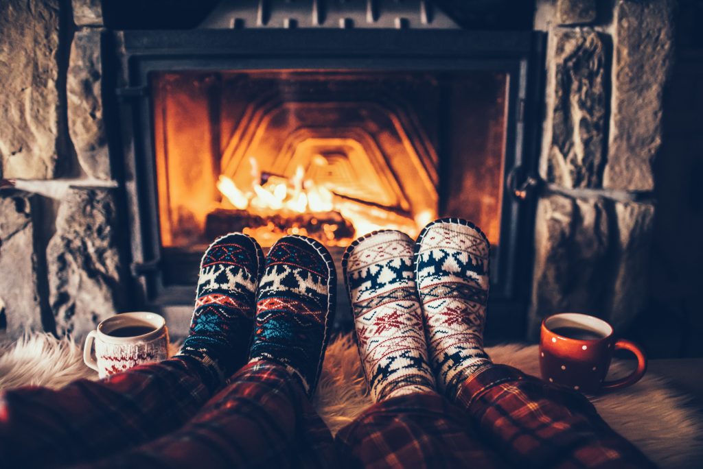 Feature of two sets of feet in Christmas socks up on coffee table in front of fireplace with hot cocoa mugs