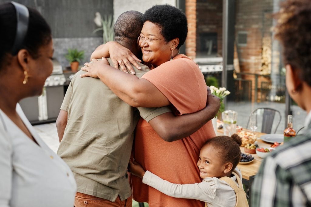 Older black couple smiling and hugging with little girl hugging around grandmother's waist.