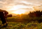 unset photo with just inset shot of young man's arm propped on bent knee holding camera with long lens, sitting, looking at sunset
