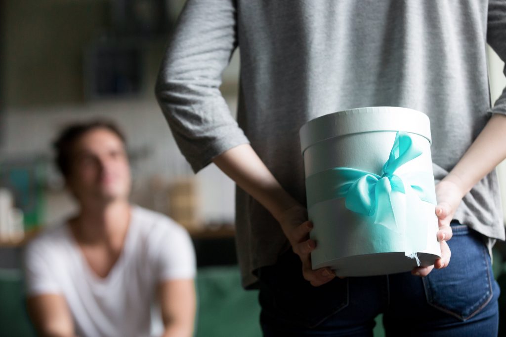 Woman hiding present behind back making romantic surprise for husband