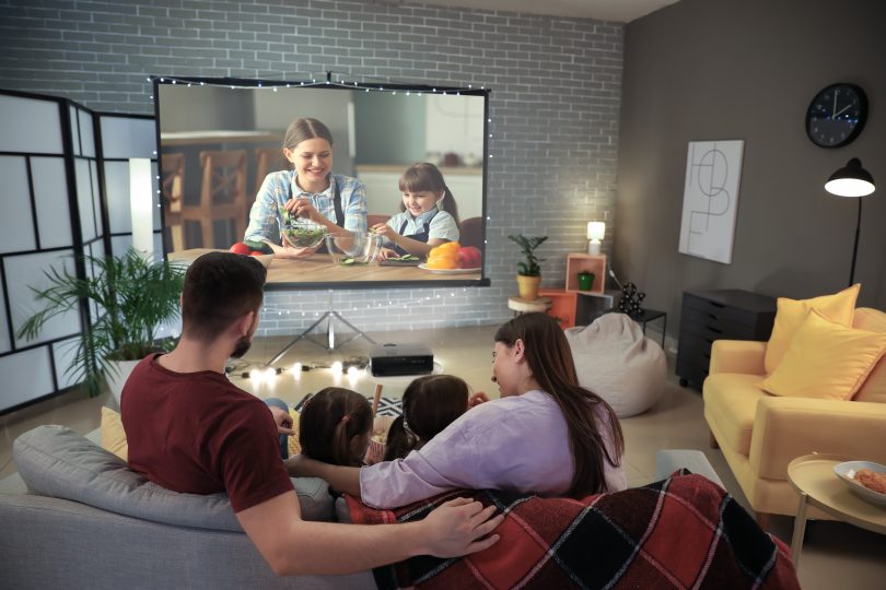Family of 4 cuddled up on sofa watching movie on home theater system