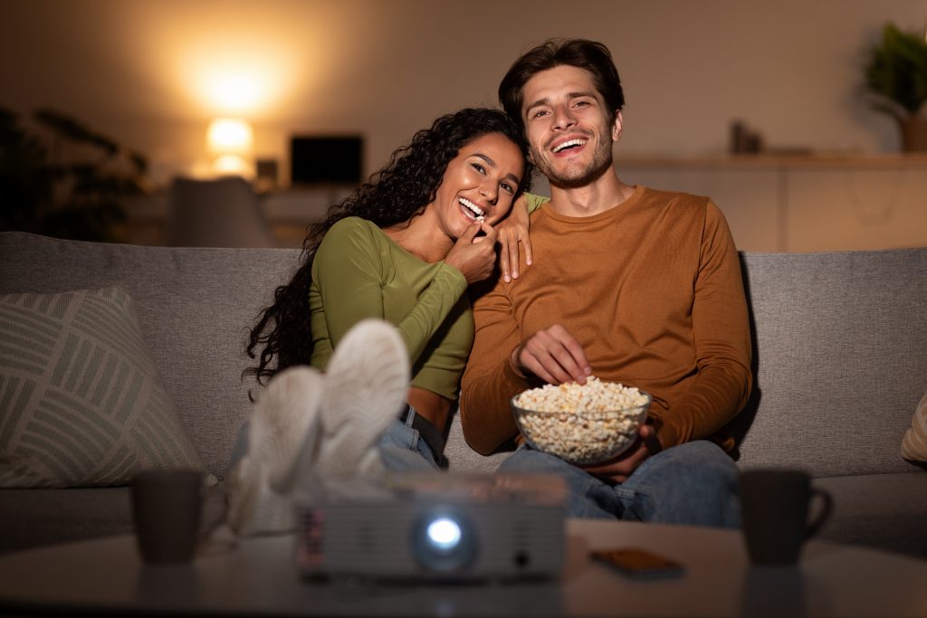 Young couple cuddled on sofa with popcorn smiling and watching movie