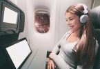 Young woman on plane with headphones and tablet