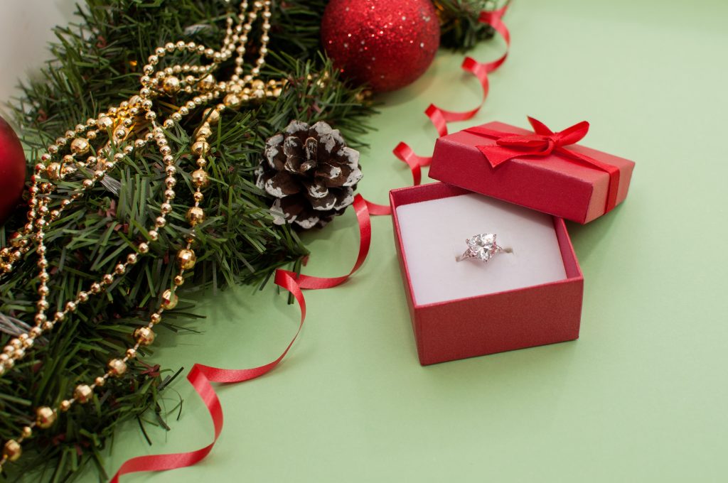 Diamond ring in red gift box next to decorated holiday garland