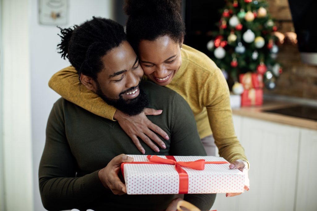 Young black couple, smiling, cheeks together, as she gives him gift