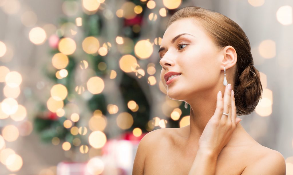 Young white woman dressed up, touching diamond earrings, holiday lights blurred behind her
