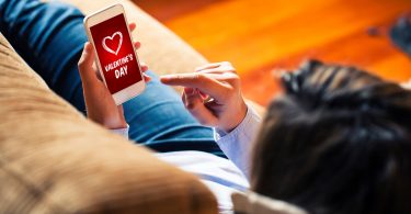 A woman lies on the sofa, browsing the FlexShopper app for Valentine's Day shopping.