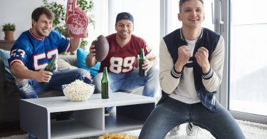 Three young male football friends watching game, rooting for team